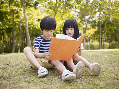 坐在草地上看书的亚洲小男孩女在公图片