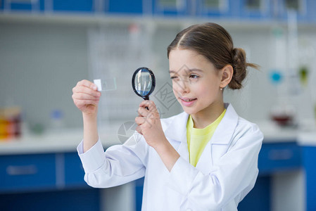 通过放大镜观察玻璃显微镜幻灯片的小女科学家背景图片