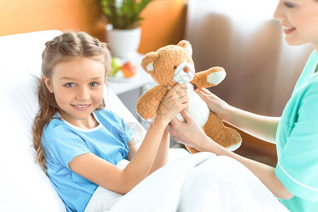 护士给医院中微笑的小女孩送泰迪熊给泰迪图片