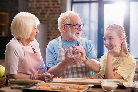 祖母祖父和孙女在厨房餐桌上烹饪和揉面团做饼干图片