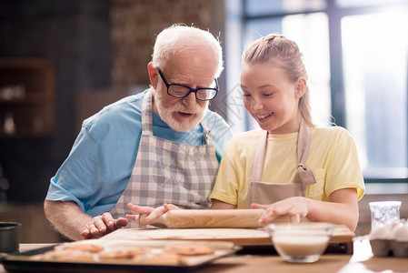 孙子和祖父用厨房用具在餐桌上烹饪和制作饼干面团图片