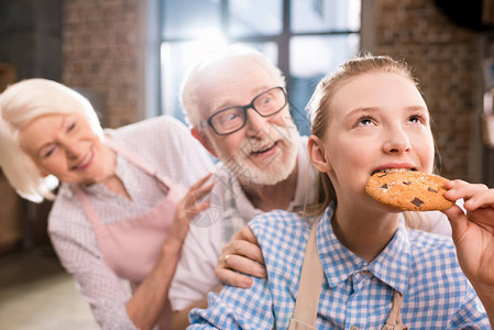 在祖父母身后吃自制饼干的女孩图片