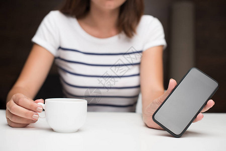 妇女用咖啡杯手持智能手机的空白屏幕所描图片
