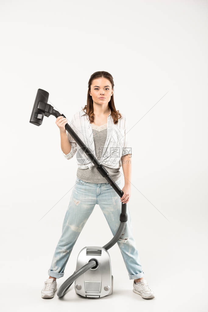 自信的年轻女站在吸尘器清洁工面前看着在白色上图片