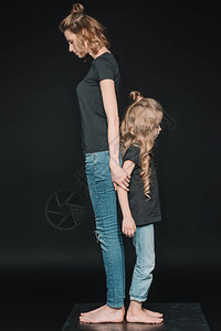 时髦的女儿和母亲的侧面背靠站在被图片