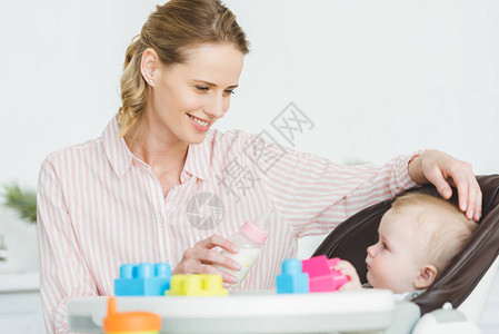 有喂奶瓶的母亲和婴儿女婴坐在婴儿椅子上图片
