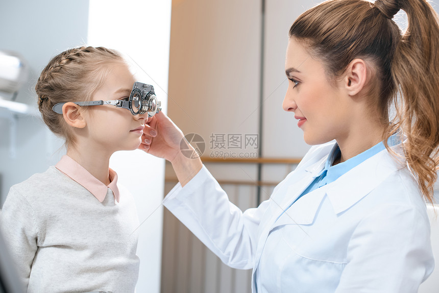 观察家在诊所用试验框架检查儿童的眼图片