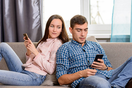 坐在沙发上用智能手机的年轻夫妇女孩通过一个手图片