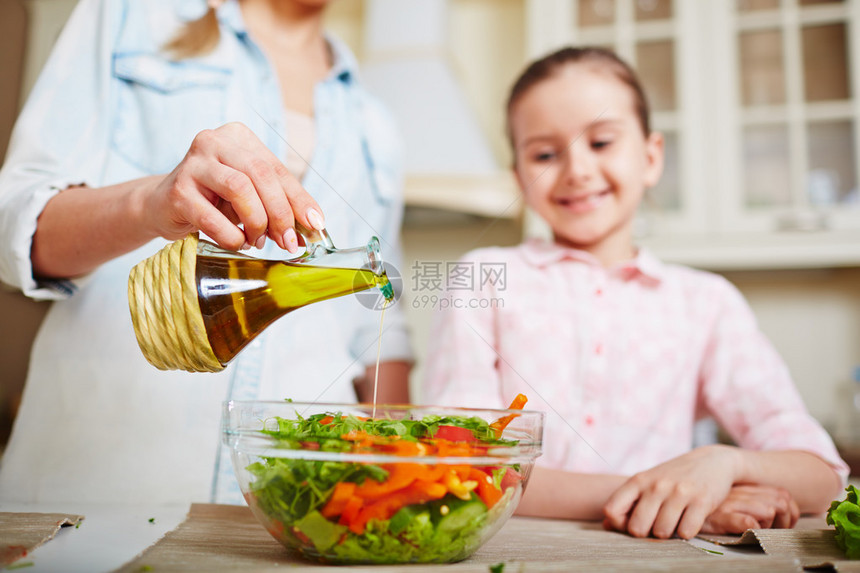 年轻女子将橄榄油滴入碗里家里厨房有图片