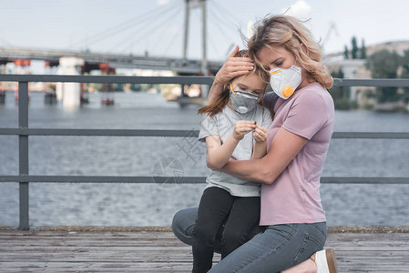 母亲戴着保护面罩抱在桥上的女儿空气污图片