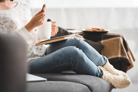 女孩在沙发上阅读书时用茶叶吃饼图片