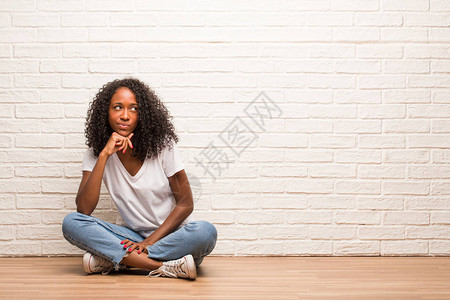 坐在木地板上思考和抬头的年轻黑人女图片