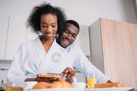 笑的非洲美国女人在吐司上撒黄油和男图片