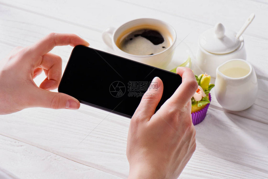 手持智能手机空白屏幕咖啡杯奶油和甜松饼在木头表面图片