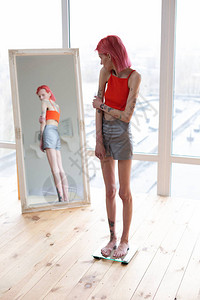 红头发的厌食女站在体重秤上看着镜图片