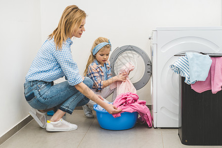 母亲和女儿在家中洗衣机中洗衣图片