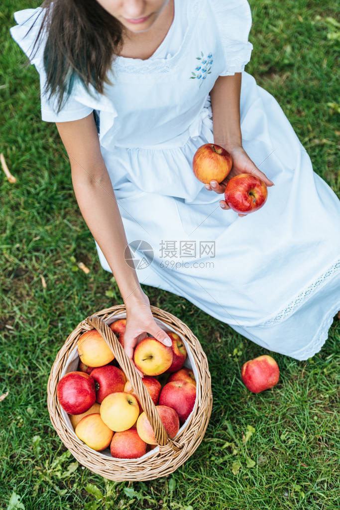坐在草地上的树枝篮子里新鲜摘苹果女孩图片