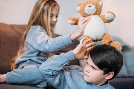 男孩和女孩在家里玩泰迪熊坐在沙发上图片