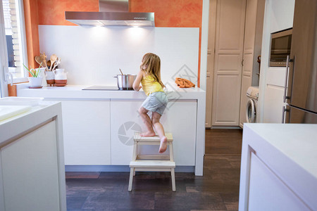 四岁金发孩子爬上凳子或梯子在电锅炉里做饭用一个酱油盆图片