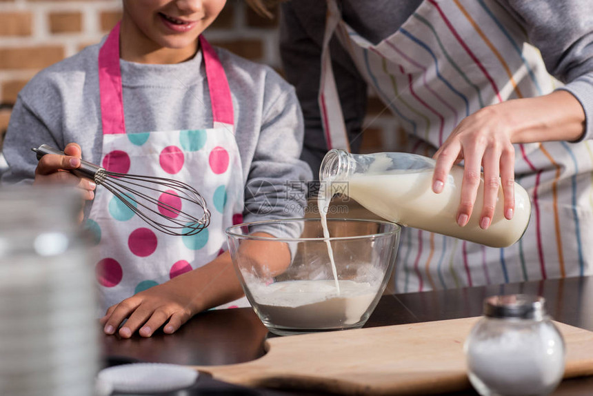 妇女与儿在家做饼干时将牛奶倒进碗中图片