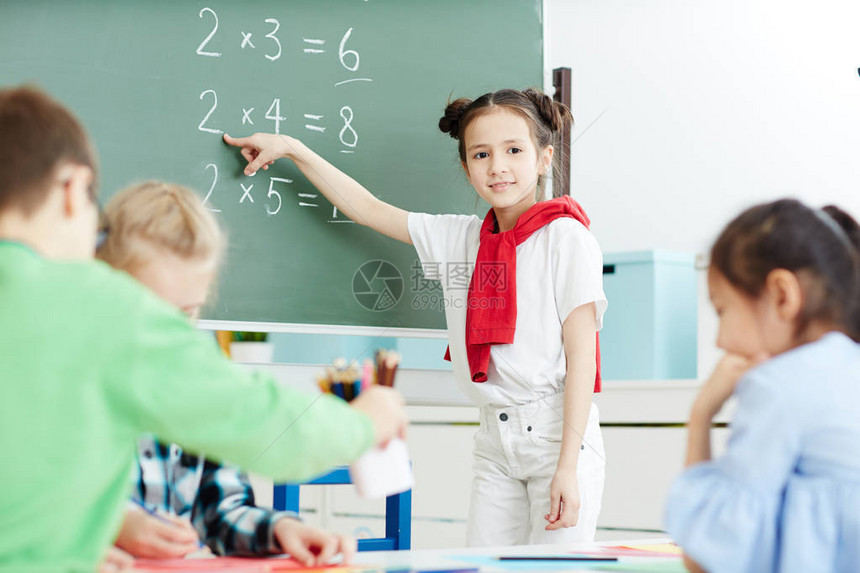 聪明的女孩站在黑板上指着数学课图片