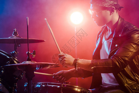 在舞台摇滚音乐会期间玩鼓的皮夹克中年轻男图片