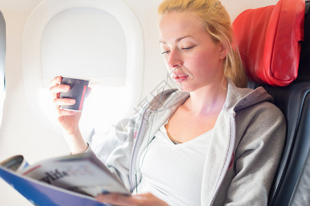 机舱内喝咖啡读杂志的女性图片