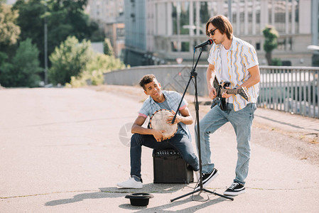 年轻快乐的男街头音乐家在城市弹吉他和图片
