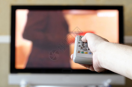 电视背景上带遥控器的手图片