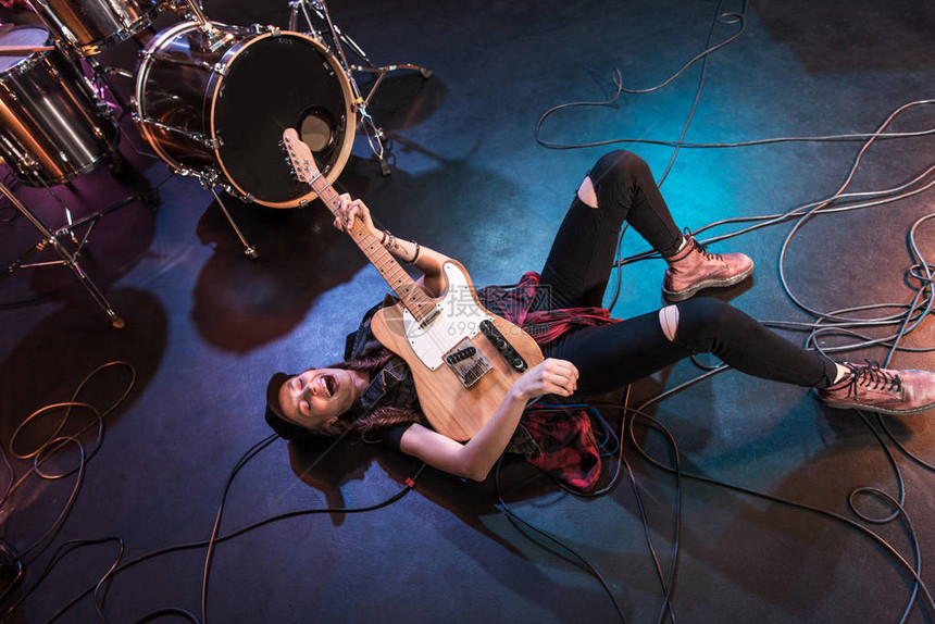 兴奋的摇滚女孩躺在舞台上用低音吉他演奏硬摇图片