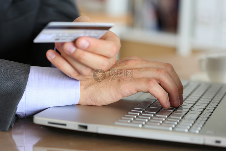穿着西装的商人手里拿着信用卡和使用笔记本电脑进行在线购买购物消费主义交付或网上银行概念反欺诈和图片
