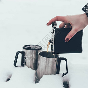 冬天在雪中将咖啡倒入杯子里的女人图片