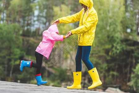 穿着雨衣和橡胶靴的母女在秋林中一起玩乐时手图片
