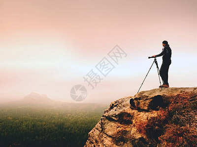 现场专业摄影师在岩石峰顶用镜子相机拍照图片