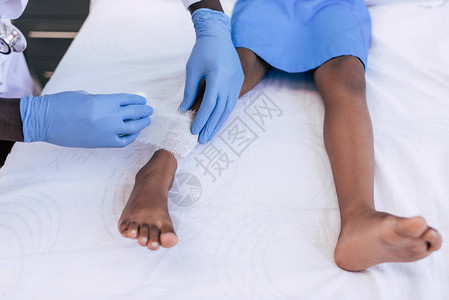 将伤腿病人的绷带贴上绷带AfricanAmerican医生用图片