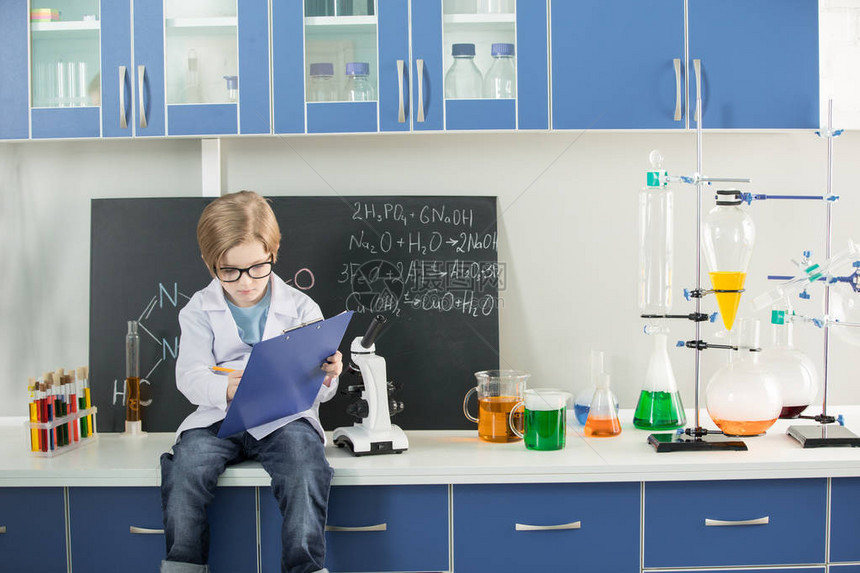 在科学实验室剪贴板上做笔记的小男孩穿图片