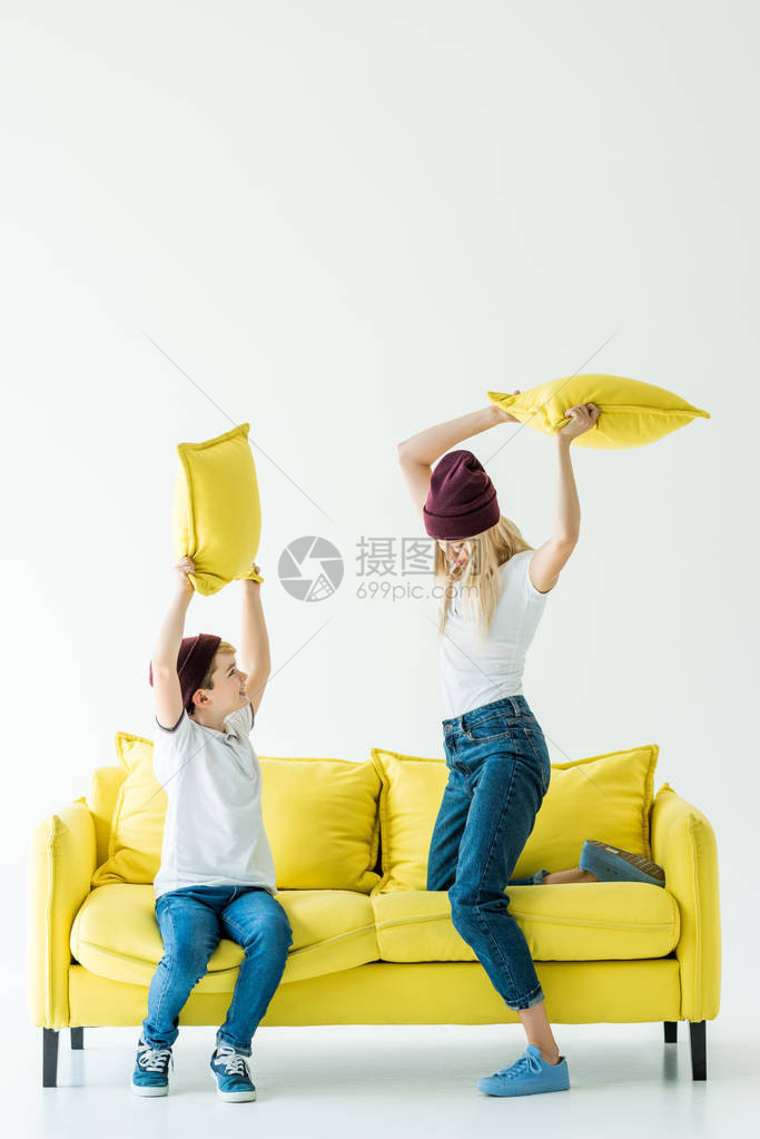 穿着便衣的母亲和儿子在白色黄沙发上与枕头打图片