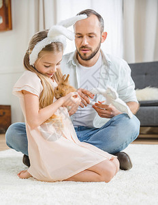 父亲和女儿坐在白地毯上玩着可爱的兔子坐图片