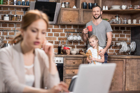 父亲和女儿用笔记本电脑在厨房白图片