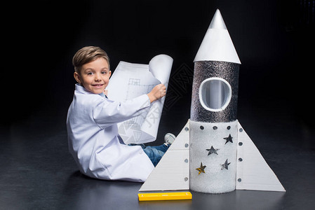 穿着白色大衣的小男孩坐在玩具火箭附近图片