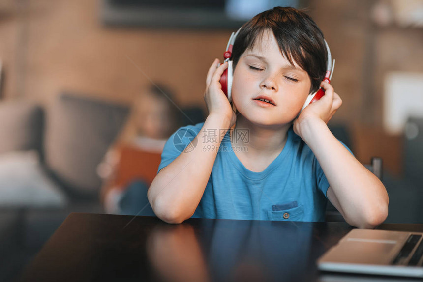 小男孩坐在家里用耳机听音乐图片