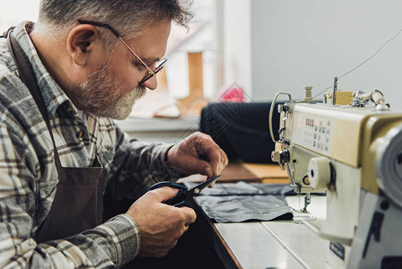 在工作室缝纫机附近用剪刀皮匠切割皮革的男手图片
