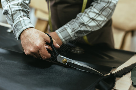 在工作室用剪刀切割皮革的男手袋工图片