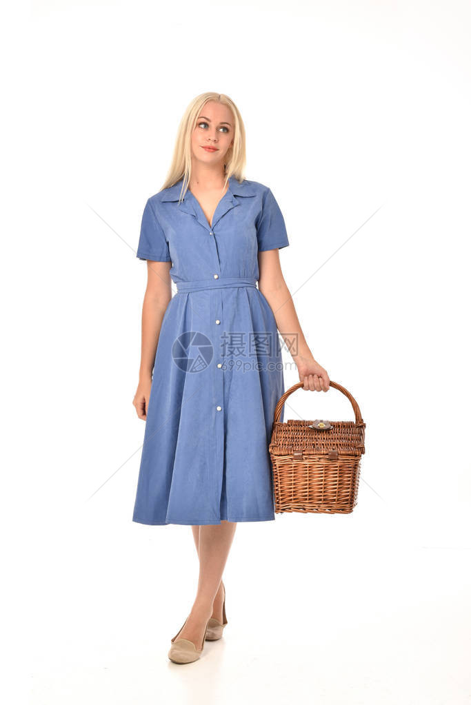 身着蓝裙子的金发女孩全长肖像拿着一个野餐篮子站立姿势在白色工作室图片