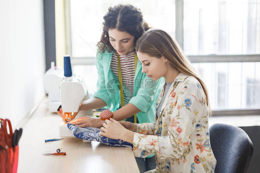 漂亮的女裁缝教女孩在现代缝纫车间用缝纫机工作图片