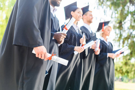持有滚版文凭的斗篷和帽子毕业学生背景图片