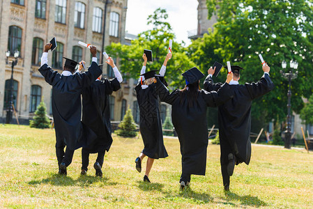 庆祝在大学花园散步的披斗篷中年轻毕业学生图片