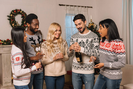 喜笑的多文化朋友与庆祝圣诞节的香槟在家中图片