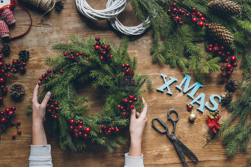 手顶上有女手握着圣诞花圈树枝和装饰浆果在木制桌面上图片
