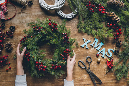 手顶上有女手握着圣诞花圈树枝和装饰浆果在木制桌面上图片